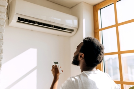 Rear view of young man turning on air conditioner at home.